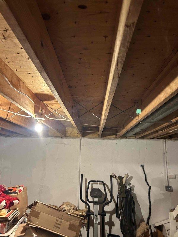 Completed sump pump relocation assessment and planning for basement drainage system. Evaluated existing sump pump discharge routing and confirmed feasibility of rerouting discharge line to front yard with placement beyond sidewalk as requested. Inspected basement ceiling structure, existing plumbing infrastructure, and discharge piping configuration to determine optimal path for new discharge line installation. Documented current system setup including exposed joists, existing pipe runs, and available routing options through photographic evidence. Prepared specifications for permanent relocation work to ensure proper drainage away from foundation while meeting municipal requirements for LFUCG compliance.