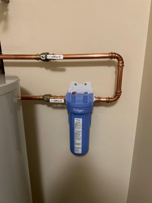 Replaced existing water heater with new Bradford White 40-gallon gas tall tank unit in residential utility closet. Installed customer-supplied in-line water filtration system with blue Culligan filter housing, integrated into copper supply line configuration using proper fittings and shut-off valves. Connected all hot and cold water lines, installed yellow flexible gas line to unit, and completed proper venting installation with gray vent piping. All connections tested and verified operational with no leaks detected.