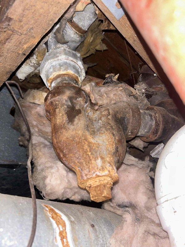 Responded to service call for clogged bathtub drain on main floor. Upon inspection, accessed plumbing infrastructure behind wall cavity and beneath structure to diagnose drainage issue. Found heavily corroded drain assembly and trap components with significant rust and oxidation buildup restricting water flow. Removed wall access panel to examine water supply lines, shut-off valves, and drainage piping. Identified deteriorated metal drain fixture as primary cause of blockage. Cleared obstruction and assessed condition of connecting PVC drainage lines and galvanized piping. Documented existing plumbing configuration including brass fixtures, PEX supply lines, and drain assembly for maintenance records. Restored proper drainage function to bathtub.