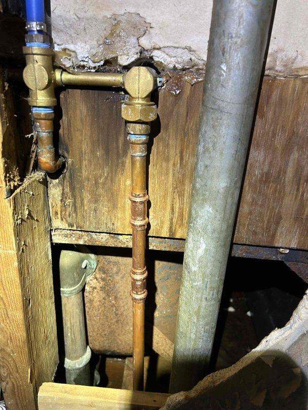 Responded to bathroom faucet leak in 1980s-era rental property. Upon inspection, traced leak source to deteriorated supply line connections in basement utility area. Identified corroded copper piping with significant oxidation and failing brass fittings at T-joint connections. Replaced compromised brass connectors and integrated new PEX supply line to existing copper infrastructure. Shut off main water supply via red-handled valves, removed damaged fittings, and installed new brass transition fittings to ensure proper connection integrity. Restored water service and tested all connections for leaks. Verified faucet operation and confirmed no active leaks in bathroom or basement area.