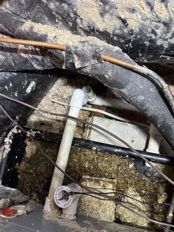 Responded to water leak complaint with HVAC system dripping through ceiling. Upon inspection, accessed unit and identified condensate drain line issue with excessive dust and debris accumulation throughout the mechanical compartment. Found PVC condensate drain line with visible valve and fittings showing signs of potential blockage or improper drainage. Documented heavily soiled conditions including thick dust buildup on flexible ductwork, refrigerant lines, and surrounding surfaces that may contribute to moisture-related problems. System currently maintaining heating and cooling functionality despite active leak. Photographed wooden shim installation between components and overall condition of confined mechanical space for records. Recommended thorough cleaning of drain line system and removal of accumulated debris to prevent future water intrusion issues.
