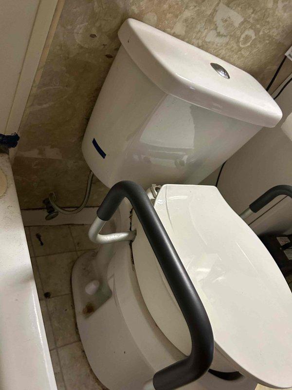 Responded to service call for non-functional toilet with disabled flush handle. Upon arrival, found water supply had been shut off due to previous flooding incident that occurred when toilet was lifted. Assessed toilet condition and accessibility features, noting wall-mounted tank configuration with safety grab bar installation. Inspected flexible water supply line connection and verified shut-off valve position. Documented existing conditions including floor tile wear patterns and overall fixture placement in accessible bathroom setting.