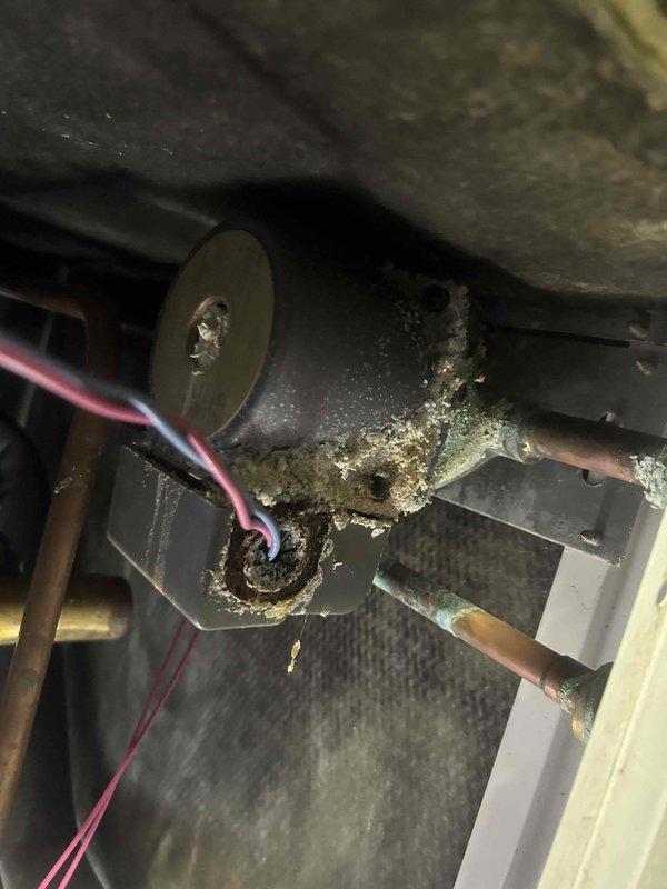 Responded to no cooling complaint on 10+ year old geothermal system located in basement. Upon inspection, discovered evaporator coil completely frozen with ice buildup on blower housing and significant condensate accumulation in drain pan. Found extensive mineral deposits and corrosion throughout unit, indicating long-term moisture issues. System was blowing air but not cooling due to frozen coil blocking airflow and heat exchange. Identified probable causes as restricted airflow from dirty coil, low refrigerant charge, or failed metering device. Shut down system to allow coil to thaw completely. Recommended thorough coil cleaning, refrigerant charge verification, and inspection of ground loop operation once thawed. Advised that geothermal systems require specialized diagnostics and that additional service will be needed to determine root cause and restore proper cooling function.