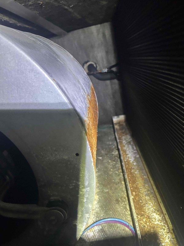Responded to no cooling complaint on 10+ year old geothermal system located in basement. Upon inspection, discovered evaporator coil completely frozen with ice buildup on blower housing and significant condensate accumulation in drain pan. Found extensive mineral deposits and corrosion throughout unit, indicating long-term moisture issues. System was blowing air but not cooling due to frozen coil blocking airflow and heat exchange. Identified probable causes as restricted airflow from dirty coil, low refrigerant charge, or failed metering device. Shut down system to allow coil to thaw completely. Recommended thorough coil cleaning, refrigerant charge verification, and inspection of ground loop operation once thawed. Advised that geothermal systems require specialized diagnostics and that additional service will be needed to determine root cause and restore proper cooling function.