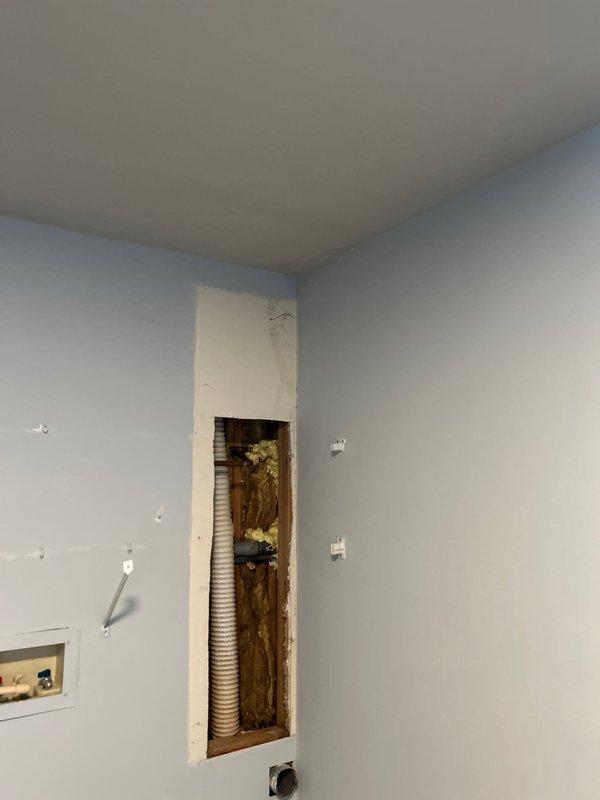 Responded to water leak originating from outdoor hose spigot penetrating into interior laundry room. Accessed wall cavity by creating drywall openings to trace leak source and assess extent of water intrusion. Located compromised connection point where exterior spigot piping penetrated wall assembly. Removed sections of drywall to expose framing, insulation, and plumbing components for proper diagnosis and repair access. Documented existing conditions including water-damaged insulation and structural framing requiring remediation.