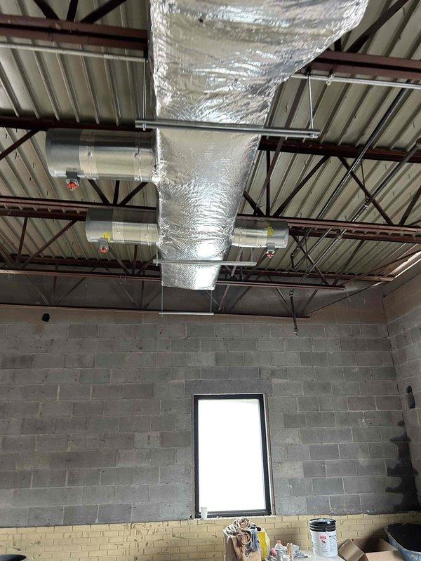 Completed commercial HVAC ductwork installation in unfinished commercial building space per approved plans. Supplied and installed all specified supply and return ductwork with reflective insulation throughout facility, including rectangular and cylindrical duct transitions suspended from exposed ceiling structure. Installed complete bathroom exhaust ductwork system. Coordinated crane services to successfully set two 7.5-ton rooftop units on building roof. Installed all grilles, registers, and diffusers as specified in project drawings. Secured all necessary permits and completed required inspections. All ductwork properly insulated and secured to structural members using appropriate hangers and supports. System ready for startup upon completion of gas piping and electrical connections by others. Project represents second phase of three-phase installation with one-year warranty on all supplied materials and labor following initial startup.