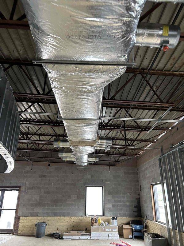 Completed commercial HVAC ductwork installation in unfinished commercial building space per approved plans. Supplied and installed all specified supply and return ductwork with reflective insulation throughout facility, including rectangular and cylindrical duct transitions suspended from exposed ceiling structure. Installed complete bathroom exhaust ductwork system. Coordinated crane services to successfully set two 7.5-ton rooftop units on building roof. Installed all grilles, registers, and diffusers as specified in project drawings. Secured all necessary permits and completed required inspections. All ductwork properly insulated and secured to structural members using appropriate hangers and supports. System ready for startup upon completion of gas piping and electrical connections by others. Project represents second phase of three-phase installation with one-year warranty on all supplied materials and labor following initial startup.