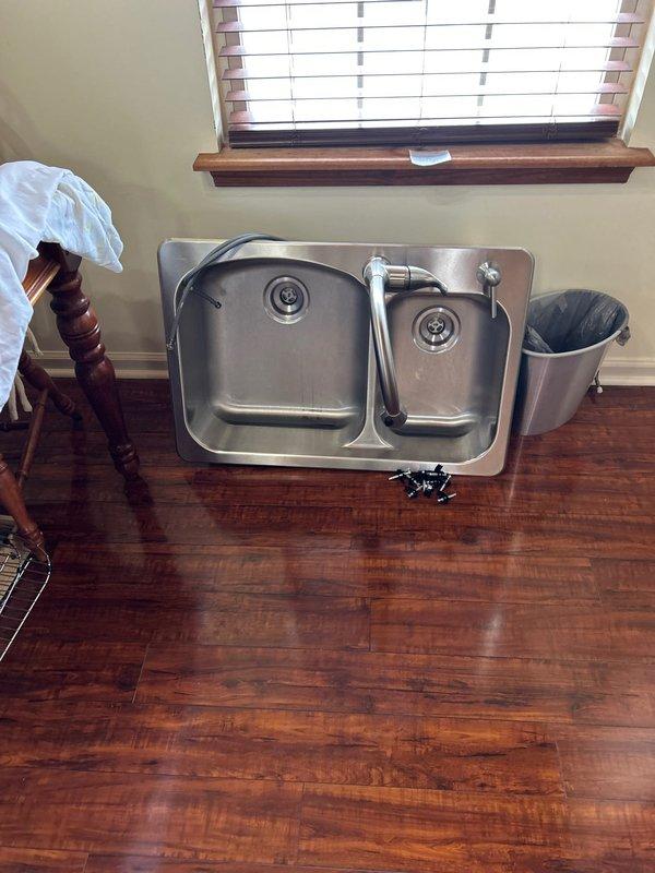 Temporarily removed previously installed stainless steel double-basin kitchen sink with chrome faucet and spray attachment to allow countertop contractor access for their installation work. Sink and fixtures were carefully disconnected and staged in protected area. Upon completion of countertop work, reinstalled kitchen sink, reconnected all plumbing lines, and verified proper drainage and water supply functionality before departure.