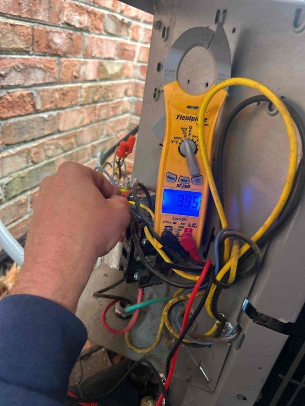 Completed scheduled preventive maintenance tune-up on approximately 10-year-old air conditioning system located in crawlspace. Performed comprehensive electrical diagnostics using digital multimeter and clamp meter on outdoor condensing unit. Verified voltage readings at electrical panel, tested capacitor operation, and measured amperage draw showing 304.5 amps on compressor circuit. Inspected all wire connections including red, black, yellow, blue, green, and white conductors at terminal block. Confirmed proper electrical values and secure connections throughout system. Customer provided their own 16x25x4 air filter as specified. System operating within normal parameters upon completion of maintenance service.