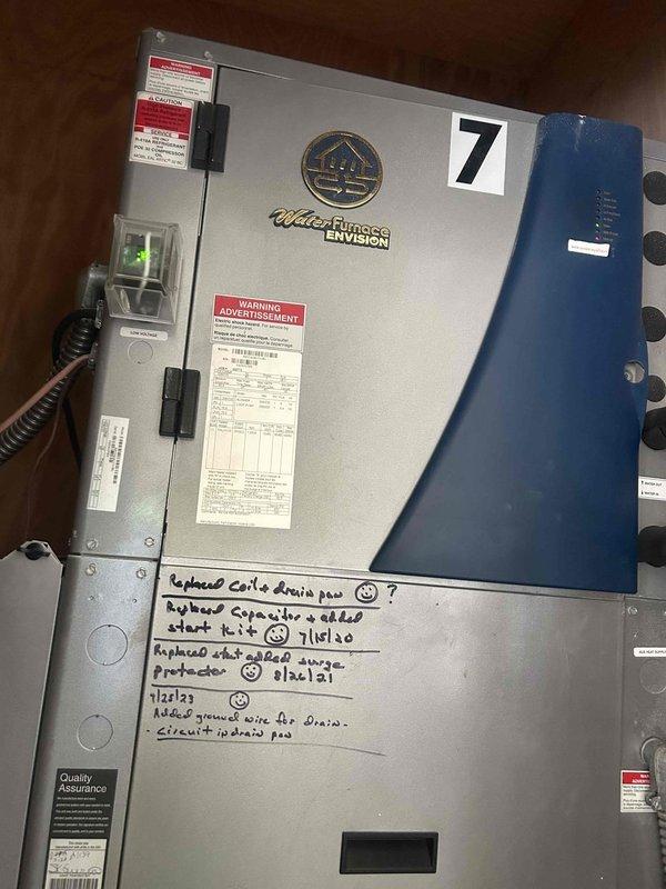 Responded to no cooling call for residential property with multiple geothermal heat pump systems. Upon arrival, found customer operates 7 WaterFurnace Envision geothermal units throughout the home. Conducted systematic inspection of units, focusing on unit #5 and unit #7 as photographed during diagnostic process. Evaluated electrical connections, control boards, and thermostat operations on affected systems. Inspected wall-mounted controls showing indicator lights and verified proper communication between thermostats and air handlers. Checked Carrier-branded air handling components and associated ductwork for airflow restrictions. Reviewed service history notations marked on equipment cabinets dating back to previous maintenance visits. Assessed geothermal loop connections and blue buffer tanks attached to units. Determined which of the 7 geothermal systems were experiencing cooling failures versus operating normally. Documented equipment conditions with photographs for service records