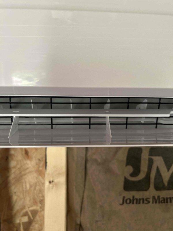 Returned to property to replace damaged bottom panel on ductless mini-split unit that was compromised during initial installation at auxiliary building beside main driveway. Retrieved replacement panel and remote control from warehouse staging area, installed new panel on wall-mounted indoor unit, and performed complete system startup and operational checkout to verify proper functionality.