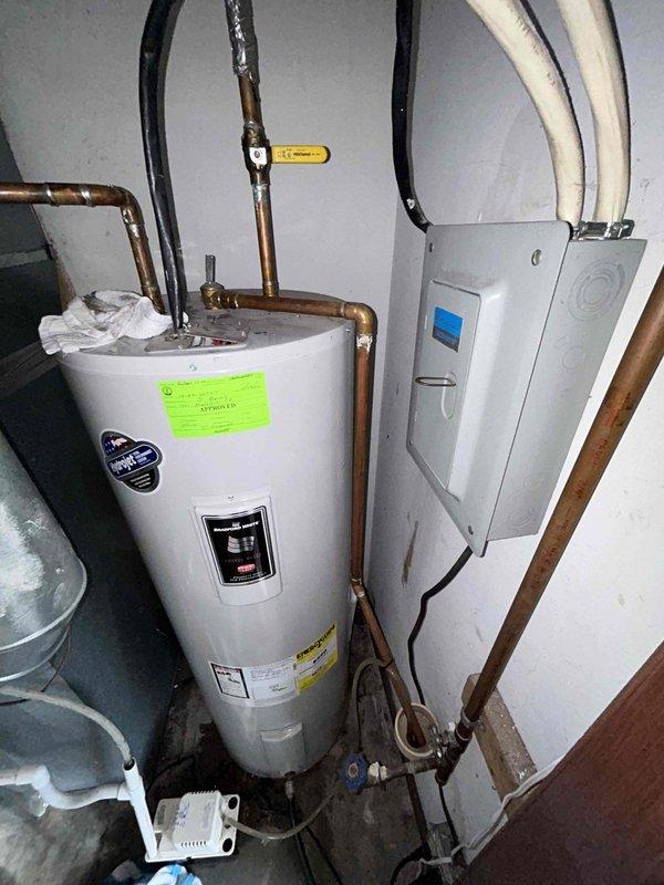 Responded to service call for 12-year-old tanked water heater in garage with no hot water and active leaking. Upon inspection, identified significant leak at upper pipe connections with visible water damage and towels placed to absorb moisture around copper piping. Assessed unit condition, noting age-related deterioration including oxidation and patina on copper lines and brass fittings. Documented equipment configuration including connections to electrical panel, multiple pipe runs (PVC and copper), and overall system layout. Photographed leak points and surrounding plumbing infrastructure for diagnostic evaluation and replacement recommendations given unit age and extent of failure.