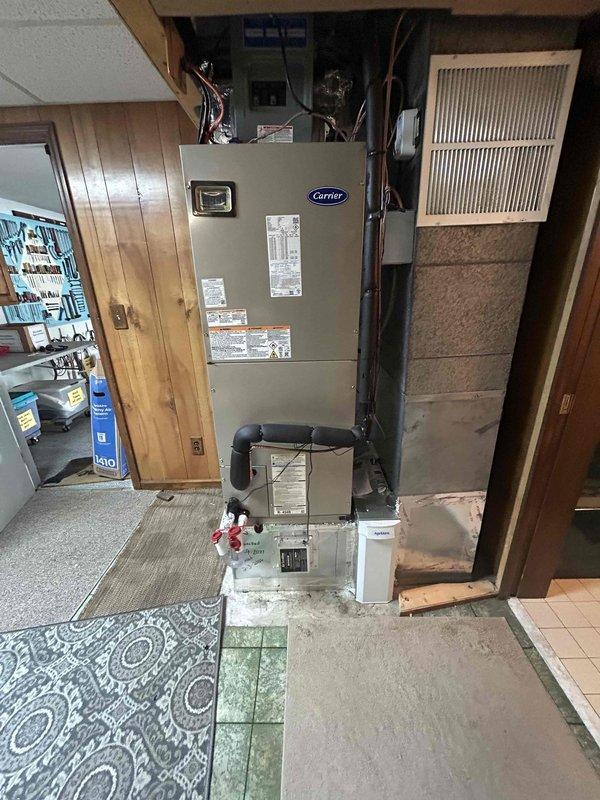 Completed full residential HVAC system replacement including installation of Carrier 3-ton 16.2 SEER2 Performance Series single-stage heat pump (model 27SPA636A003) on concrete pad with snow legs and electrical disconnect box in backyard against brick exterior wall. Installed Carrier 3-ton air handler with variable speed blower (model FT5ANXC36L00) in basement utility area with 15kW electric heat kit (model AFAEHL15B01A) and Carrier thermostat control. Added Aprilaire media cabinet air filtration system and condensate pump for proper drainage management. Ran insulated refrigerant lines with inline filter connecting outdoor condenser to indoor air handler, installed electrical whip kit and disconnect box for code compliance. Integrated SS2 coil drain safety water sensor with trap, fabricated transitions to existing ductwork system, and removed/disposed of old equipment. Pulled all applicable permits, tested system operation including heating and cooling modes, verified proper airflow an