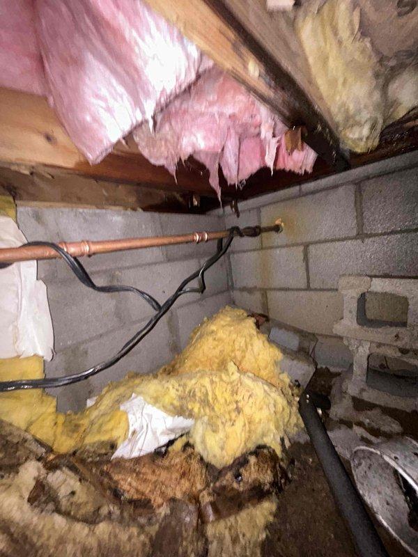 Responded to emergency plumbing service call for active water leak in crawlspace that was causing excessive runtime on spring pump. Located source of dripping leak on copper piping in crawlspace area where heat tape had been previously installed during winter months. Accessed confined crawlspace area with exposed floor joists, concrete block foundation walls, and existing fiberglass insulation. Inspected copper pipe runs and identified leak at pipe coupling/connector joint. Removed deteriorated and water-damaged insulation material from affected area to access leak point. Repaired leaking copper pipe connection to stop active drip and prevent further water accumulation in crawlspace. Verified repair held pressure and leak was fully resolved to prevent continued strain on spring pump system.
