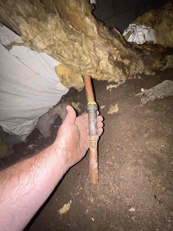 Responded to emergency plumbing service call for active water leak in crawlspace that was causing excessive runtime on spring pump. Located source of dripping leak on copper piping in crawlspace area where heat tape had been previously installed during winter months. Accessed confined crawlspace area with exposed floor joists, concrete block foundation walls, and existing fiberglass insulation. Inspected copper pipe runs and identified leak at pipe coupling/connector joint. Removed deteriorated and water-damaged insulation material from affected area to access leak point. Repaired leaking copper pipe connection to stop active drip and prevent further water accumulation in crawlspace. Verified repair held pressure and leak was fully resolved to prevent continued strain on spring pump system.