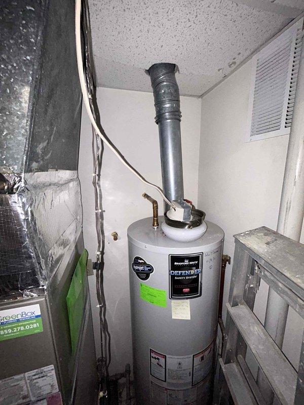 Responded to water leak emergency affecting main floor utility area where ceiling had collapsed from steady water intrusion. Water supply was shut off upon arrival to prevent further damage. Inspected mechanical room containing water heater, HVAC equipment, and associated plumbing systems to identify leak source originating from upper level. Documented conditions of Bradford White Defender water heater, air handler unit, PVC condensate lines with safety switch, and copper supply lines. Placed collection vessel beneath affected area and assessed extent of water damage to ceiling structure and mechanical equipment below.