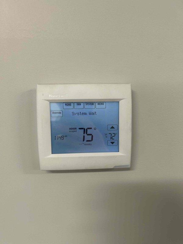 Responded to no cooling complaint in front office area of commercial facility. Upon arrival, found Honeywell programmable thermostat displaying "System: Wait" message with indoor temperature reading 75°F and setpoint at 72°F. Inspected thermostat operation and checked battery backup compartment, which contained two AA batteries. System appeared to be in delay mode following power interruption or recent thermostat adjustment. Verified thermostat was receiving power and communicating properly with split system air handler located in warehouse closet. Cycled system through operational modes to clear wait delay and restore normal cooling function to affected office space.