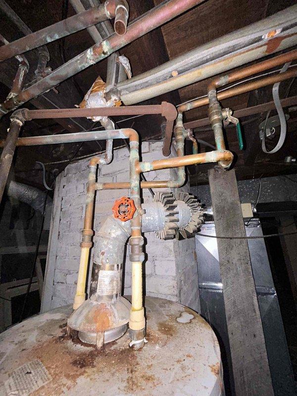 Responded to service call for older tanked water heater in basement with no hot water production. Upon inspection, found severely corroded and aged plumbing infrastructure with extensive oxidation on copper piping, shut-off valves, and connections throughout the system. Water heater tank displayed significant rust staining and deterioration consistent with age-related failure. Assessed circulator pump assembly, piping network, and heat exchanger components showing advanced wear and mineral deposit accumulation. Documented existing conditions including compromised valve operation due to corrosion buildup and overall system degradation requiring replacement recommendation.