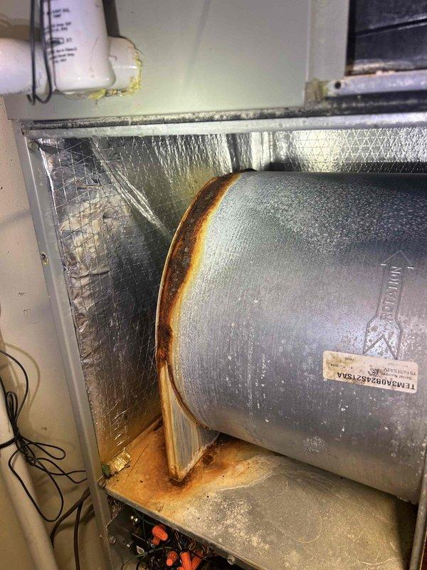 Responded to water leak complaint at indoor AC unit located in utility room. Upon inspection, discovered extensive water damage and rust corrosion throughout the air handler cabinet, with significant staining on reflective insulation and interior surfaces indicating prolonged moisture exposure. 

Identified primary issue as condensate drainage system failure causing water to overflow onto floor. Blower compartment showed evidence of standing water with rust streaking down cabinet walls and deterioration of wooden platform supporting blower assembly. Condensation visible on supply duct confirmed active moisture problem.

Inspected condensate drain line, drain pan, and associated plumbing connections for blockages or damage. Evaluated blower motor and electrical connections for water damage exposure. Documented extensive rust damage to cabinet interior and insulation materials requiring attention to prevent further deterioration and potential system failure.

Photographed damage for reco