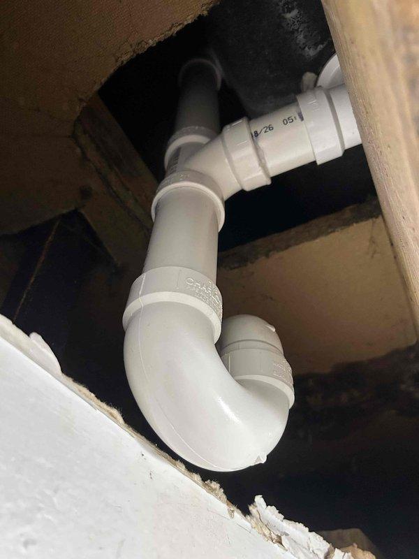 Removed existing P-trap assembly and installed new white PVC trap configuration beneath floor structure, accessible through ceiling opening. Installed new drain assembly with proper 90-degree elbows and coupling sections to ensure correct drainage flow. Tested all connections and joints for leaks upon completion, confirming watertight seal throughout the entire plumbing assembly.