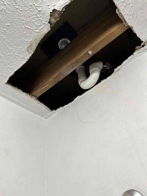 Removed existing P-trap assembly and installed new white PVC trap configuration beneath floor structure, accessible through ceiling opening. Installed new drain assembly with proper 90-degree elbows and coupling sections to ensure correct drainage flow. Tested all connections and joints for leaks upon completion, confirming watertight seal throughout the entire plumbing assembly.