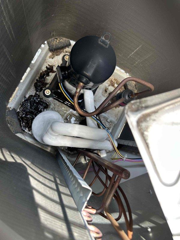 Responded to no cooling call on commercial HVAC system. Upon arrival, performed diagnostic inspection of outdoor condensing unit and indoor air handler components. Inspected compressor, refrigerant lines, electrical connections, and condensate drainage system. Photographed equipment condition showing normal operational wear on copper refrigerant lines and accumulation of debris in drain pan. Verified proper installation of insulated refrigerant piping and assessed overall system configuration. Condensing unit located on exterior gravel pad with weathered copper lines and black insulation showing age-appropriate condition. Indoor equipment positioned in metal drain pan with visible dirt accumulation requiring attention. Documented current state of mechanical components, electrical wiring connections, and condensate management system for diagnostic evaluation and recommended maintenance procedures.