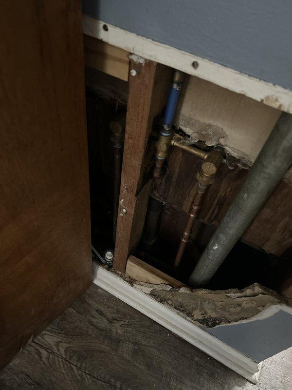 Responded to intermittent water leak originating from upstairs bathroom and affecting downstairs bathroom ceiling. Accessed wall cavity and identified water-stained structural components and plumbing connections. Located source of leak at supply valve assembly between floor joists, where brass valve fitting and PVC pipe connections showed evidence of moisture infiltration and rust staining. Documented plumbing configuration and compromised areas for repair recommendations.
