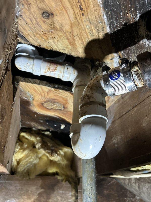 Responded to intermittent water leak originating from upstairs bathroom and affecting downstairs bathroom ceiling. Accessed wall cavity and identified water-stained structural components and plumbing connections. Located source of leak at supply valve assembly between floor joists, where brass valve fitting and PVC pipe connections showed evidence of moisture infiltration and rust staining. Documented plumbing configuration and compromised areas for repair recommendations.