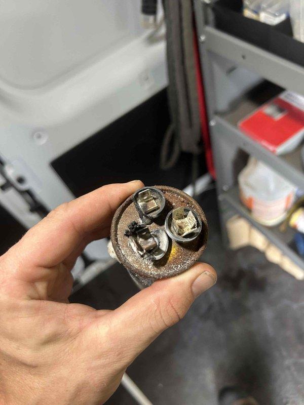 Responded to no-cooling call on 10-year-old air conditioning system. Found outdoor condensing unit humming but failing to start, with indoor unit circulating unconditioned air. Diagnosed failed dual-run capacitor with severe corrosion and rust on terminal cap, preventing compressor and condenser fan motor operation. Removed defective capacitor and installed new replacement unit with proper microfarad rating. Verified compressor startup, confirmed condenser fan motor operation, and tested system performance. Unit returned to normal cooling operation with proper amperage draw on all components.