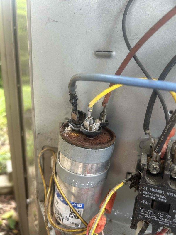 Responded to no-cooling call on 10-year-old air conditioning system. Found outdoor condensing unit humming but failing to start, with indoor unit circulating unconditioned air. Diagnosed failed dual-run capacitor with severe corrosion and rust on terminal cap, preventing compressor and condenser fan motor operation. Removed defective capacitor and installed new replacement unit with proper microfarad rating. Verified compressor startup, confirmed condenser fan motor operation, and tested system performance. Unit returned to normal cooling operation with proper amperage draw on all components.