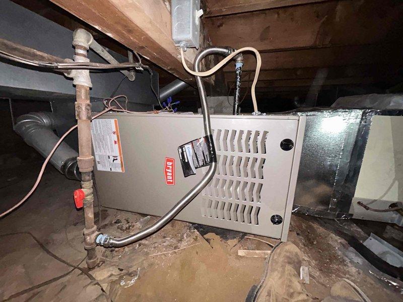 Successfully installed a Bryant Legacy 800SB36070M17 70,000 BTU 80% AFUE single-stage gas furnace in horizontal right configuration within crawl space. Removed and properly disposed of existing equipment, then positioned new unit on dirt floor beneath floor joists with appropriate clearances. Connected gas supply line with shutoff valve, installed copper refrigerant lines, and routed condensate drain tubing. Configured venting system per code requirements using single-wall 4" vent pipe with one elbow inside cabinet transitioning immediately to double-wall vent pipe, ensuring no wires or materials contacted vent components within unit cabinet. Connected supply and return ductwork using metallic flex duct with proper insulation. Completed all electrical connections and verified proper operation of blower motor, gas valve, and ignition system. Obtained necessary permits and ensured installation met all applicable building and mechanical codes for residential HVAC systems.