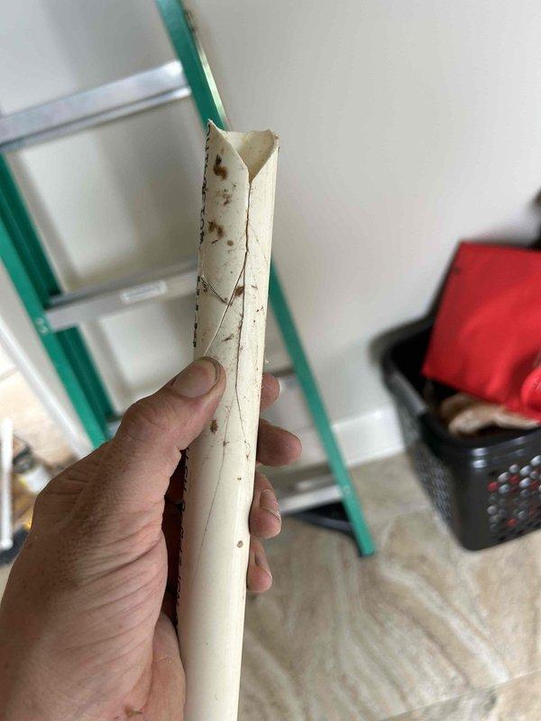 Responded to water leak emergency at attic-mounted indoor unit where condensate drain line failure caused overflow and significant ceiling damage in main bedroom. Upon inspection, discovered primary condensate drain line had completely deteriorated and split longitudinally, resulting in catastrophic failure and water discharge into living space. Removed and documented failed PVC drain section showing extensive brown staining, structural collapse, and material degradation. Replaced damaged condensate drain line with new PVC piping, ensuring proper pitch and secure connections. Verified drain flow and system operation. Unit returned to normal operating condition with proper condensate drainage restored.