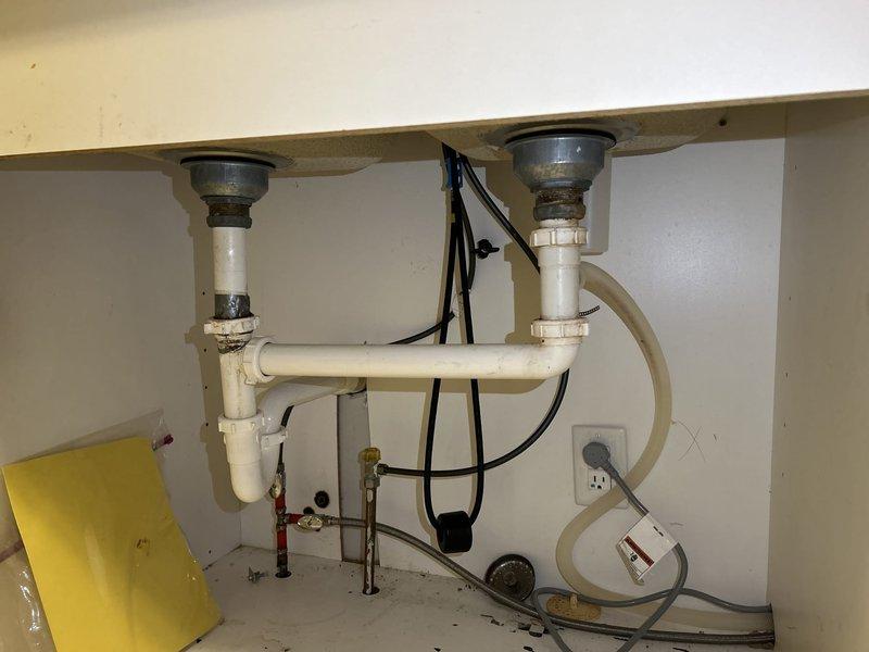 Performed comprehensive camera inspection of plumbing system to assess multiple issues. Documented kitchen sink drain assembly showing dual-basin PVC trap configuration with visible age-related deterioration and intermittent dishwasher connection leaks. Inspected bathroom toilet exhibiting water leakage around base with supply currently shut off, indicating probable wax ring failure requiring replacement. Evaluated exterior hose bibb positioned too low for standard hose connection, requiring relocation or adjustment for proper functionality.