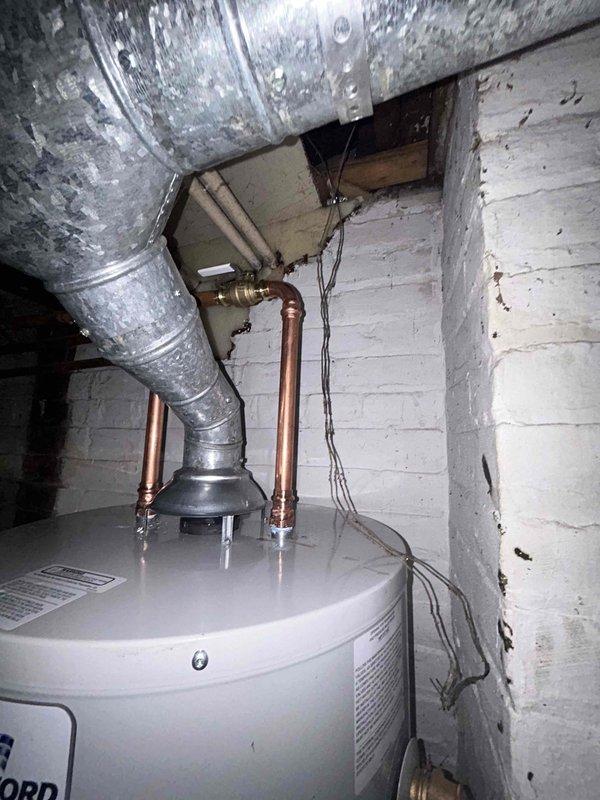# Tanked Water Heater Service Call

Responded to a no hot water complaint on a tanked water heater less than 10 years old located in the basement. Upon arrival, found significant water accumulation on the concrete floor throughout the mechanical room, with visible staining and moisture indicating an active or recent leak. Inspected two white cylindrical water heaters positioned side by side along with associated plumbing infrastructure including copper supply lines, brass fittings, and overhead piping systems.

Conducted thorough visual assessment of both water heater units, examining tank integrity, connection points, pressure relief valve operation, and all visible plumbing connections. Evaluated the copper piping configuration extending from the water heater tops, checking for corrosion, loose fittings, or signs of failure at junction points. Inspected the condition of the flexible ductwork connections and verified proper installation of all mechanical components in the utility spac