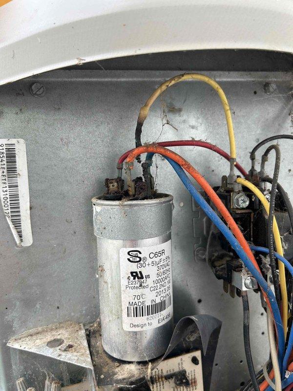 Responded to no cooling call on electric air conditioning unit located in back barn. Upon inspection, found failed run capacitor with visible heat damage to connected wiring and significant debris accumulation within electrical compartment. Replaced defective capacitor, cleaned electrical connections, removed dust and lint buildup from control panel, and verified proper system operation with all components functioning normally.