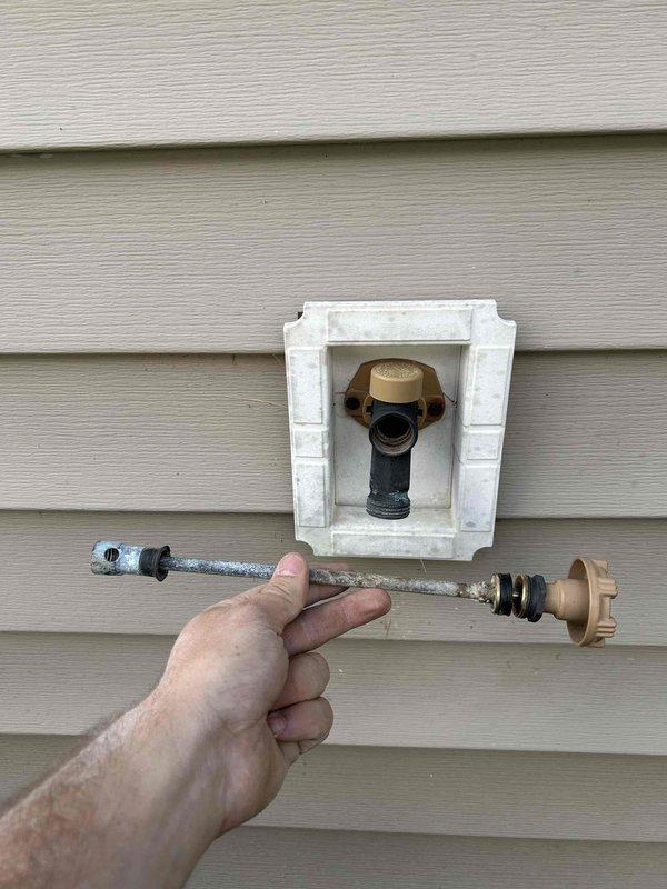 Responded to outdoor hose faucet leaking when turned on, with water escaping behind exterior vinyl siding and infiltrating interior laundry and utility rooms. Performed inspection and confirmed failed hose bib connection within wall cavity. Removed defective outdoor spigot assembly from recessed faucet box mounted on exterior wall, which showed corrosion and mineral deposits on threaded pipe section and deteriorated brass fittings. Replaced faulty hose bib with new frost-proof sillcock assembly, ensuring proper sealing at wall penetration point to prevent future water intrusion. Verified interior shutoff valve operation and tested new installation under full water pressure with no leakage detected at exterior mounting point or behind siding. Confirmed repair resolved water infiltration issue affecting interior spaces.