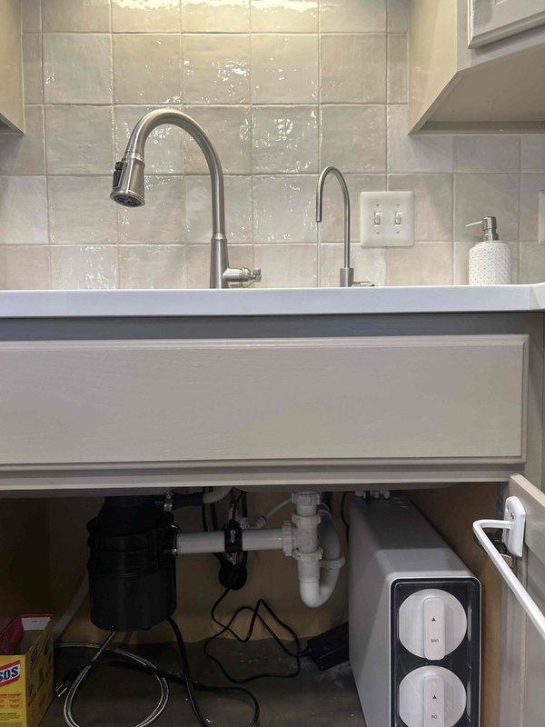 Supplied and installed a new Aqua Flo tankless reverse osmosis drinking water system beneath the kitchen sink. The installation included mounting the RO unit in the cabinet, connecting it to the existing cold water supply line, routing purified water to a dedicated gooseneck faucet installed on the countertop, and establishing proper drain connections to the existing P-trap assembly. All plumbing connections were secured and tested for leaks, with the system positioned to allow adequate clearance around the existing garbage disposal unit and drainage configuration.