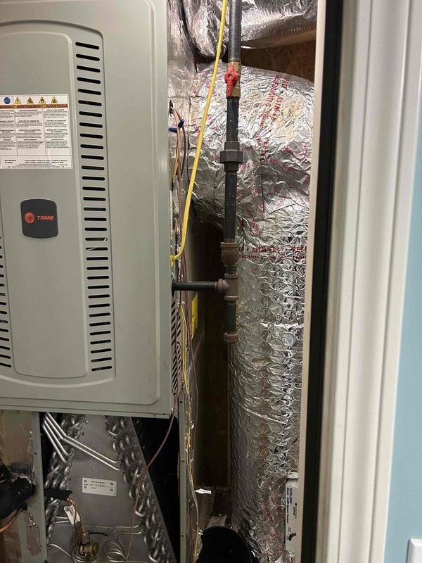 Responded to no cooling complaint on 5-year-old Trane air conditioning unit located in upstairs bathroom mechanical closet. Upon arrival, performed diagnostic inspection of system including air handler, ductwork, and condensate drain lines. Inspected vertical HVAC equipment installation, examined heat exchanger coil assembly, and verified proper mounting and connections of all components. Documented system configuration with metallic insulated ductwork, black PVC condensate piping with multiple couplings, and electrical conduit routing. System evaluated and customer advised of findings.