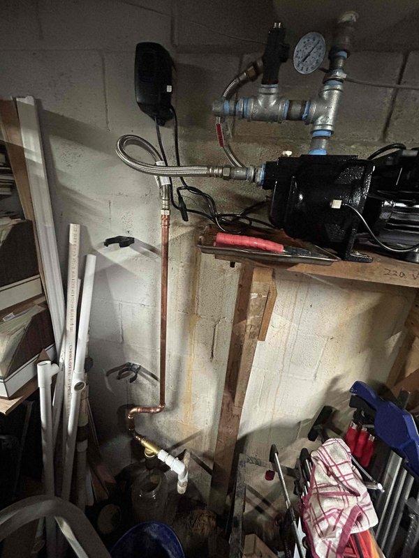 Responded to emergency water leak call involving private well water system. Upon arrival, found pump had overheated and was unplugged, with evidence of water spillage throughout basement area. Homeowner reported rust sediment clots passing through plumbing system prior to discovering water throughout lower level. Inspected well pump assembly, pressure tank, and associated copper supply lines showing significant rust and oxidation. Documented corroded piping, deteriorated pump components, and water-damaged tank with visible rust staining. System currently not operational with no active water flow. Identified failing well pump as primary issue, with secondary concerns regarding corroded distribution piping and sediment contamination from well source. Photographed pump assembly, pressure gauge, braided supply lines, and storage tank condition for documentation. No active leak present at time of inspection. Recommended pump replacement and evaluation of well water quality to address rust c