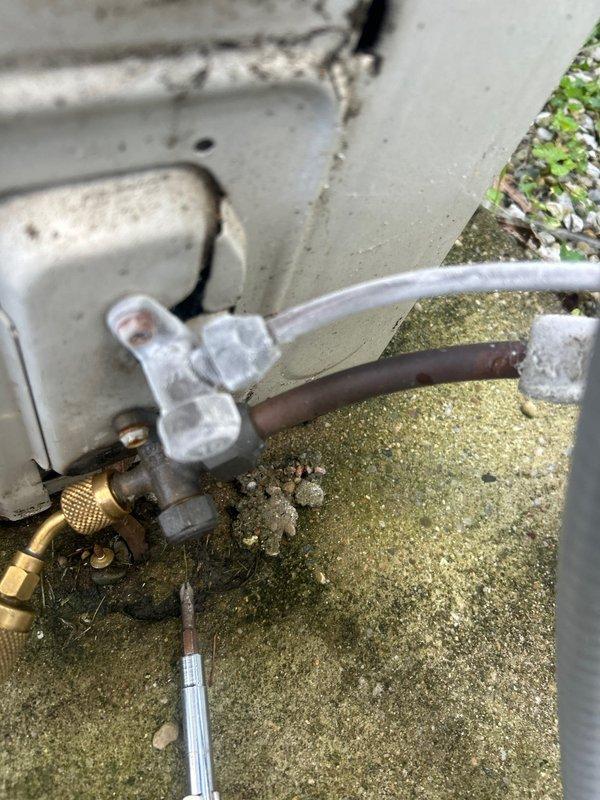 Responded to service call for mini split system in attic producing loud clanking noise during operation. Performed diagnostic inspection of indoor air handler unit and outdoor condensing unit. Examined refrigerant line connections, mounting hardware, and internal components for loose parts or debris. Outdoor unit displayed significant weathering with algae growth on concrete pad and aged brass service valves. Inspected compressor mounts, fan blades, and condenser coil for mechanical issues causing abnormal noise. Checked refrigerant lines for proper securing and vibration dampening. Documented equipment condition with photographs showing exterior connections, copper refrigerant lines with brass fittings, electrical disconnect, and general outdoor unit installation. System assessed for potential causes including loose fan assembly, failing compressor mounts, or debris in blower wheel.