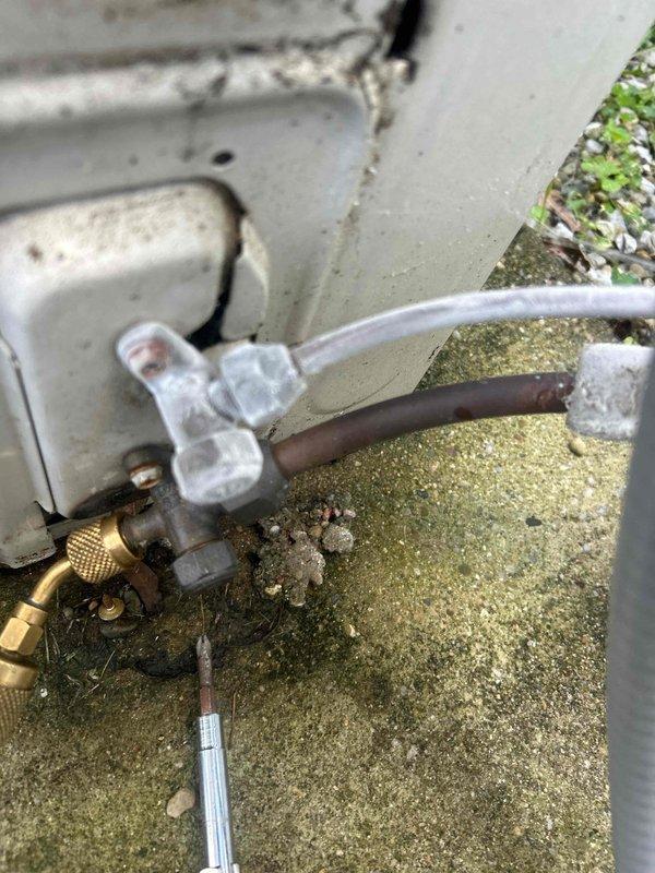 Responded to service call for mini split system in attic producing loud clanking noise during operation. Performed diagnostic inspection of indoor air handler unit and outdoor condensing unit. Examined refrigerant line connections, mounting hardware, and internal components for loose parts or debris. Outdoor unit displayed significant weathering with algae growth on concrete pad and aged brass service valves. Inspected compressor mounts, fan blades, and condenser coil for mechanical issues causing abnormal noise. Checked refrigerant lines for proper securing and vibration dampening. Documented equipment condition with photographs showing exterior connections, copper refrigerant lines with brass fittings, electrical disconnect, and general outdoor unit installation. System assessed for potential causes including loose fan assembly, failing compressor mounts, or debris in blower wheel.