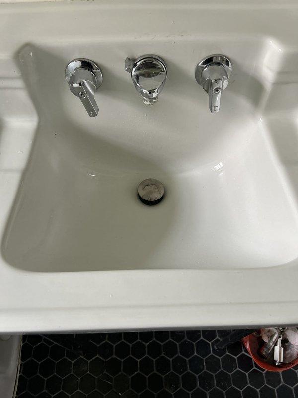 Responded to water leak complaint at main floor bathroom sink. Upon arrival, inspected geometric basin sink with wall-mounted chrome faucet assembly and documented conditions with photographs. Customer reported leak occurs only when water is running, requiring bucket placement to catch water. 

Examined drain assembly from below, inspecting chrome P-trap, black plastic tailpiece, threaded couplings, and wall-mounted shut-off valves for hot and cold water supply lines. Assessed all visible plumbing connections, drainage system components, and fixture mounting points to identify source of active leak during water flow.