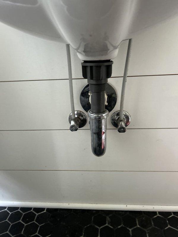 Responded to water leak complaint at main floor bathroom sink. Upon arrival, inspected geometric basin sink with wall-mounted chrome faucet assembly and documented conditions with photographs. Customer reported leak occurs only when water is running, requiring bucket placement to catch water. 

Examined drain assembly from below, inspecting chrome P-trap, black plastic tailpiece, threaded couplings, and wall-mounted shut-off valves for hot and cold water supply lines. Assessed all visible plumbing connections, drainage system components, and fixture mounting points to identify source of active leak during water flow.