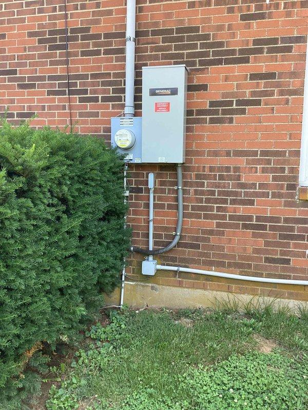 Responded to service call for Generac whole-house generator displaying red indicator light that had previously shown green status. Upon arrival, performed comprehensive diagnostic evaluation of the generator system and associated electrical components. Inspected the generator control panel, verified all electrical connections at the exterior-mounted Generac transfer switch and metering equipment, and assessed the overall installation integrity. Checked generator battery voltage, control board status indicators, and examined all visible wiring conduits for damage or loose connections. Evaluated the fuel supply system and confirmed proper grounding of the unit. Documented current system status with photographic evidence showing the exterior electrical installation including the transfer switch mounted on brick exterior wall and associated utility connections. Provided customer with diagnostic findings and recommended next steps for restoring generator to normal operational status with gr