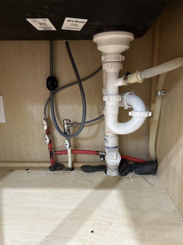 Installed new matte black pull-down kitchen faucet with gooseneck design on newly installed white quartz countertop with black composite undermount sink. Connected water supply lines to shut-off valves, installed stainless steel drain assembly with P-trap configuration using white PVC piping, and applied silicone sealant around faucet base and sink perimeter to ensure proper waterproofing.