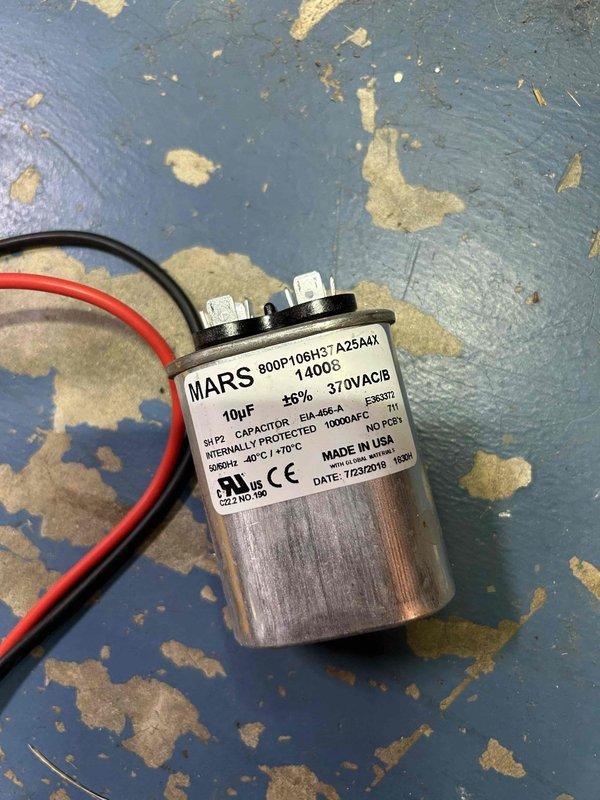 Responded to a no cooling complaint on a 19-year-old gas electric air conditioning system. Upon inspection, discovered the outdoor unit capacitor had failed, preventing the compressor and condenser fan from operating properly. Measured supply temperature at 54 degrees, confirming inadequate cooling performance. Replaced the defective dual-run capacitor with a new MARS 10µF 370VAC capacitor, restored power to the unit, and verified proper system operation with normal compressor and fan motor function.