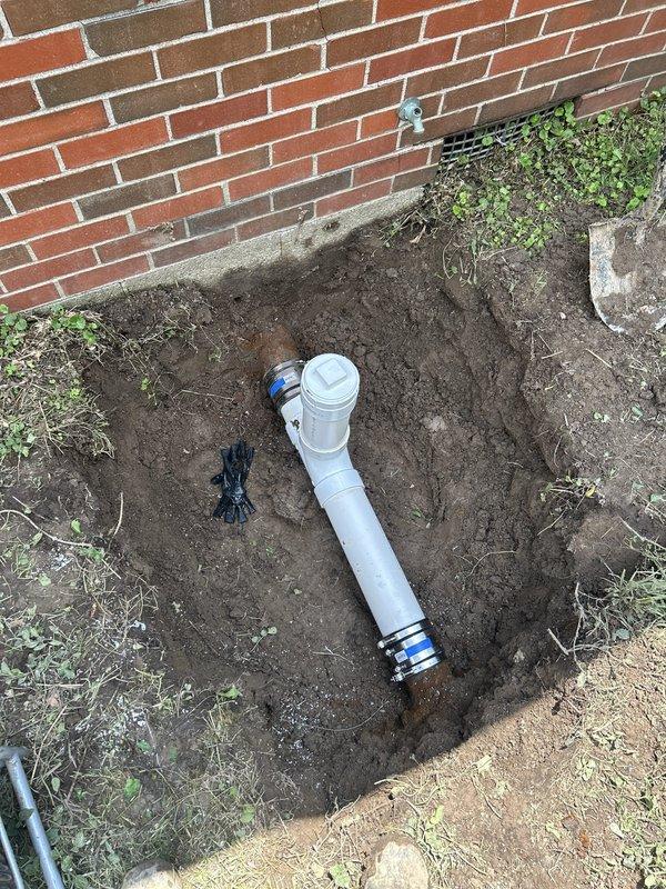 Excavated access point at building foundation and installed exterior PVC cleanout assembly with proper fittings and connections to existing sewer line. Completed underground plumbing installation to provide accessible maintenance point for future sewer line servicing and inspection capabilities.