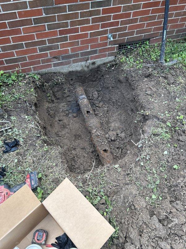 Excavated access point at building foundation and installed exterior PVC cleanout assembly with proper fittings and connections to existing sewer line. Completed underground plumbing installation to provide accessible maintenance point for future sewer line servicing and inspection capabilities.