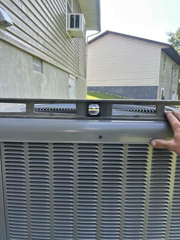 Responded to callback for tilted outdoor HVAC unit. Upon arrival, used level to assess condenser positioning and confirmed unit had settled and was no longer level. Documented current condition of RUUD outdoor unit with photographs showing degree of tilt and positioning in relation to pad. Unit requires releveling or pad adjustment to prevent potential compressor damage and ensure proper refrigerant flow and drainage.