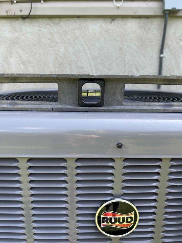 Responded to callback for tilted outdoor HVAC unit. Upon arrival, used level to assess condenser positioning and confirmed unit had settled and was no longer level. Documented current condition of RUUD outdoor unit with photographs showing degree of tilt and positioning in relation to pad. Unit requires releveling or pad adjustment to prevent potential compressor damage and ensure proper refrigerant flow and drainage.